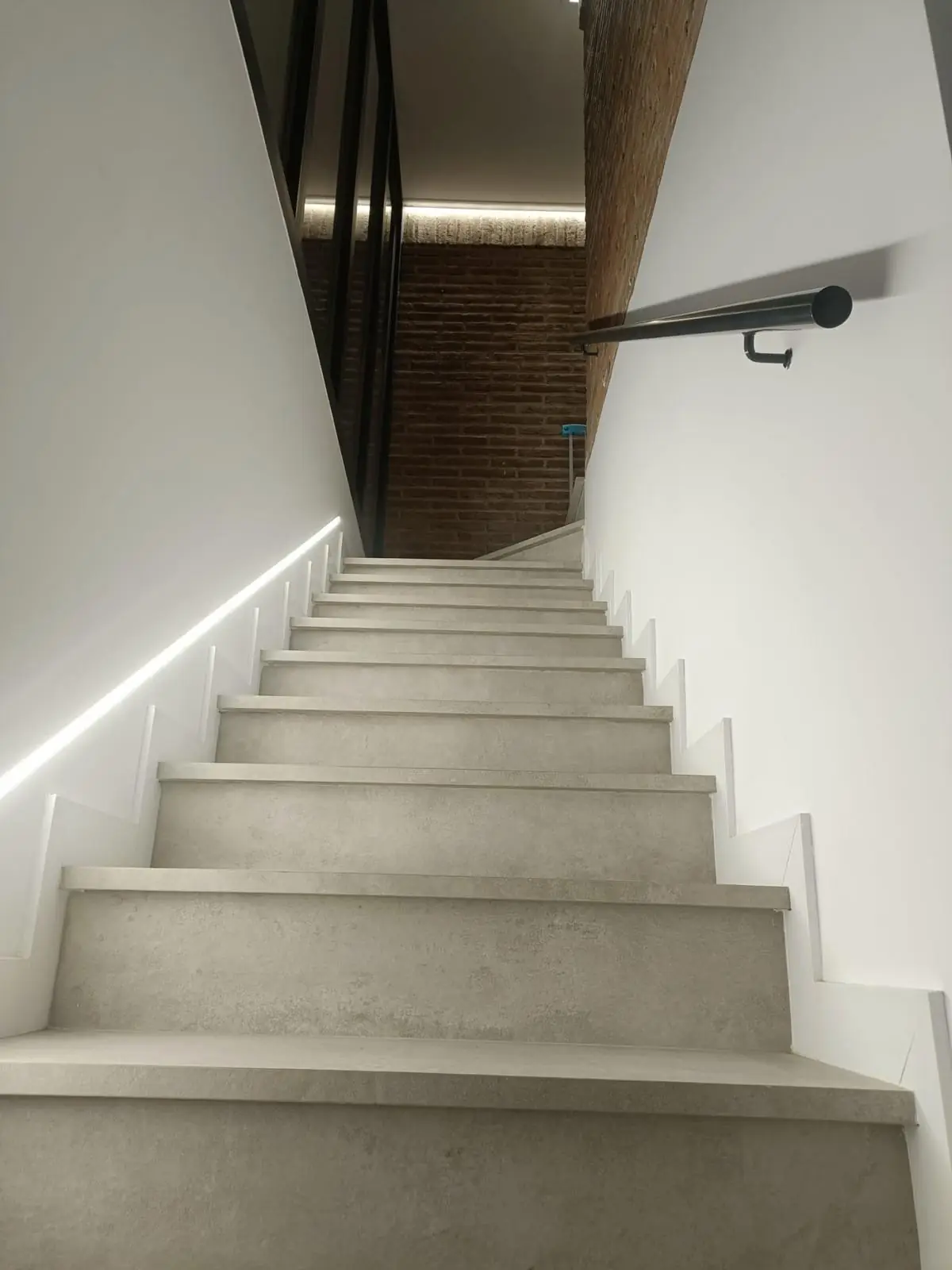 Escalera con peldaños porcelánicos e iluminación LED en el zócalo