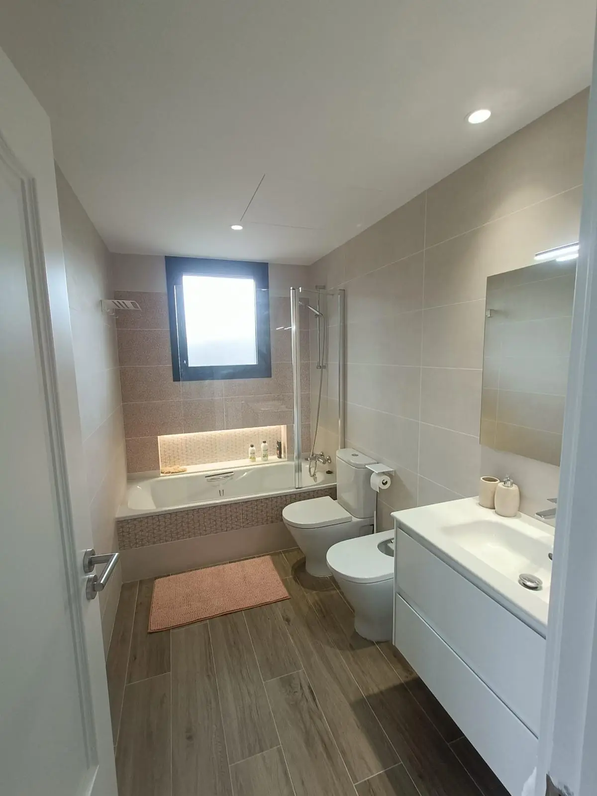 Baño completo con bañera, hornacina iluminada y mueble blanco