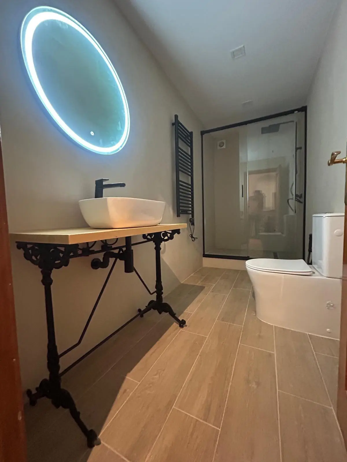 Baño con lavabo sobre encimera de madera, pie de forja y espejo con luz LED