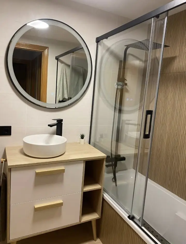Baño con mueble de madera, mampara corredera y espejo redondo